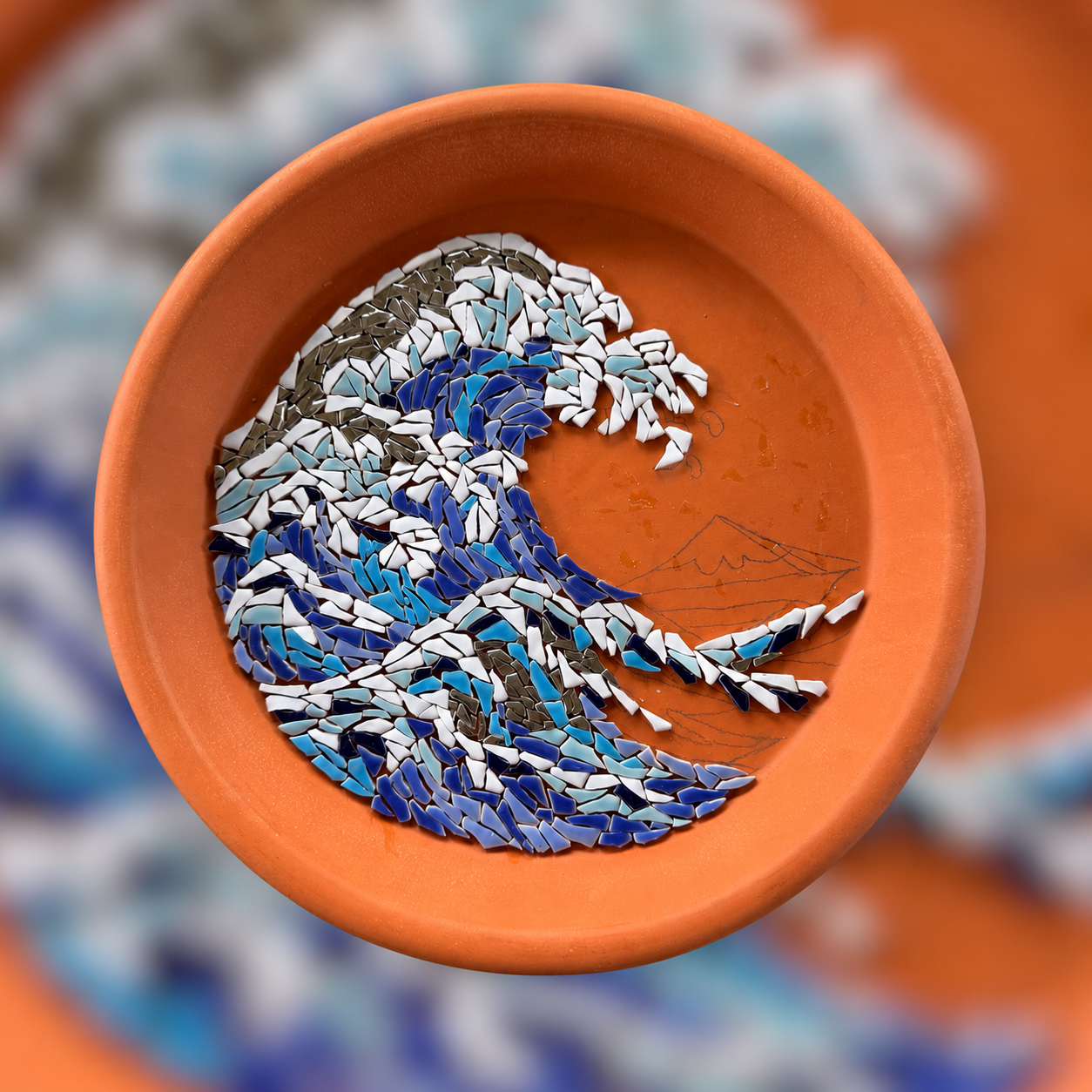 Unfinished blue and white wave mosaic with pencil outlines in a terracotta dish